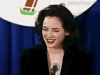 a woman is smiling while standing in front of a microphone in front of a blue curtain .