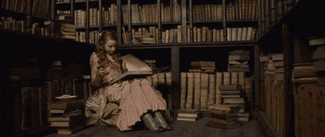 a girl in a pink dress sits on the floor reading a book