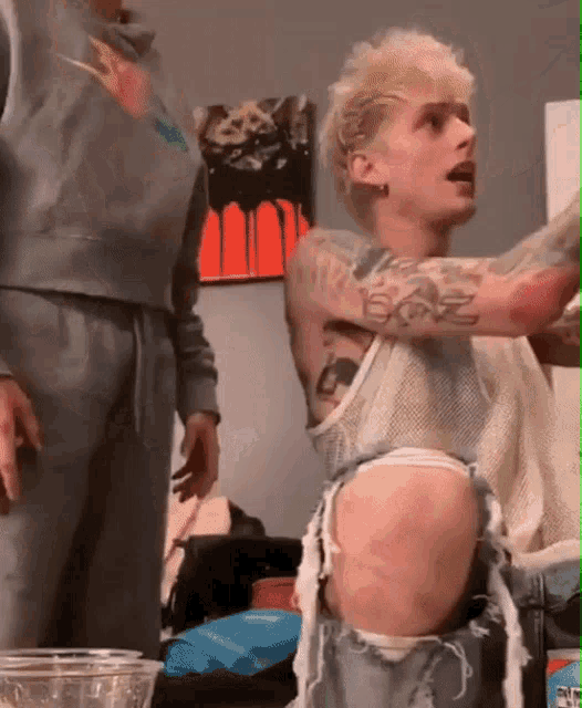 a man with a lot of tattoos on his arms and legs is sitting in a room .