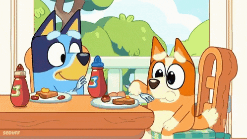 two dogs are sitting at a table eating food .