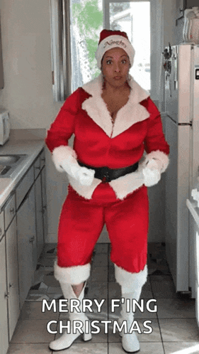 a woman in a santa costume is standing in a kitchen and says merry fing christmas