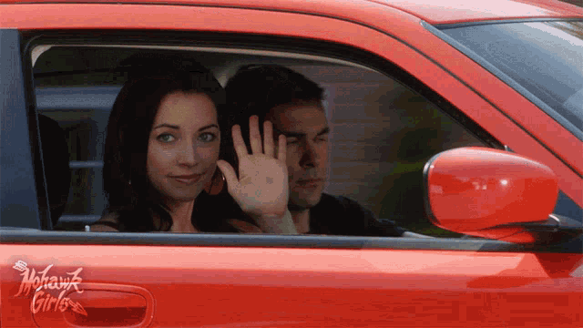 a man and a woman are sitting in a red car with a sticker on the side that says mohawk girls