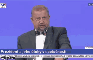 a man in a suit and bow tie is on a news channel talking about president a jeho ulohy v spolucnosti