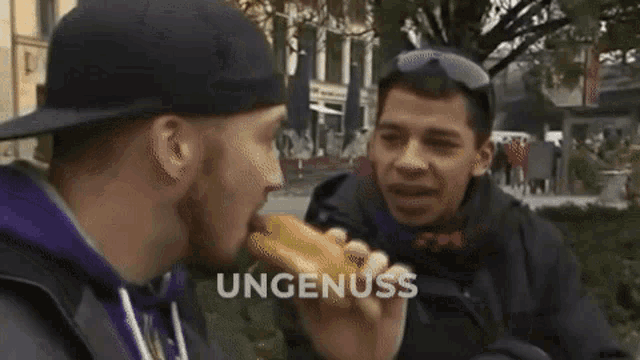 a man eating a hot dog with the word ungenuss on the bottom left