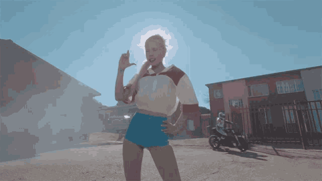 a woman in shorts and a white shirt is dancing in front of a motorcycle