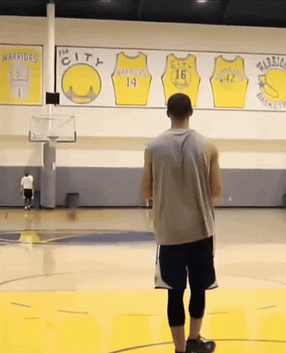 a man stands on a basketball court in front of a wall with warriors jerseys on it