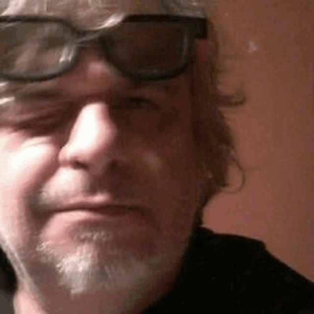 a man with a beard wearing sunglasses and a black shirt is looking at the camera .
