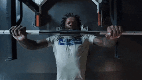 a man in a kansas shirt is lifting a barbell over his head