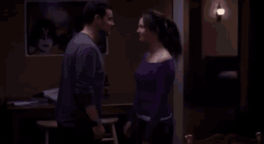 a man and a woman are standing next to each other in a dark room . the woman is wearing a purple shirt .