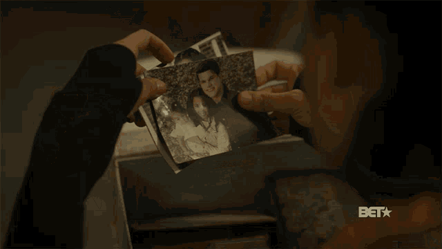a person is holding a picture of a man and woman with a baby and the bet logo is visible behind them