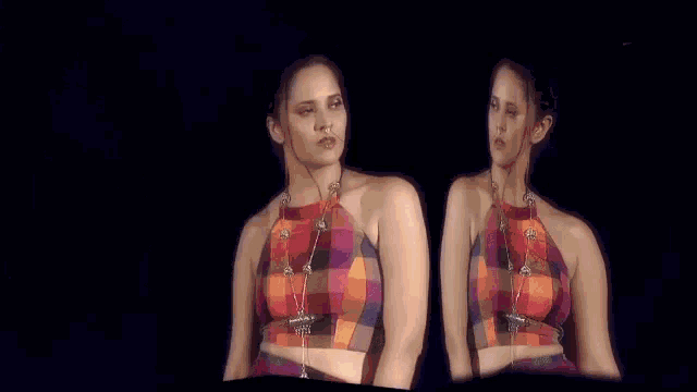 a woman in a plaid crop top is standing on a stage in front of a blue background .