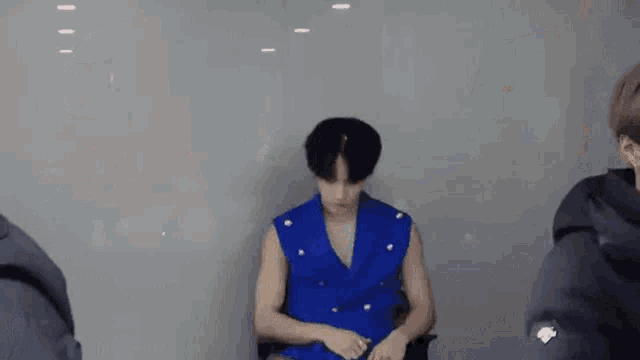 a man in a blue vest is sitting in a chair and talking to another man .
