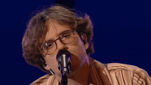 a man singing into a microphone with glasses on