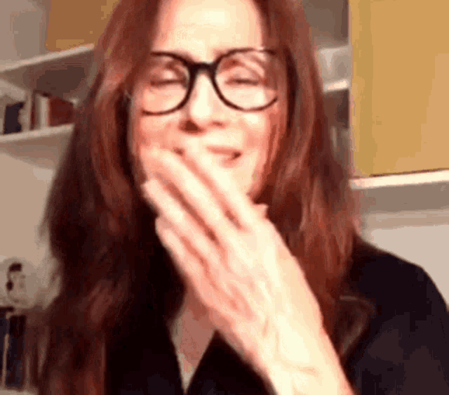 a woman with red hair wearing glasses is covering her mouth with her hand .