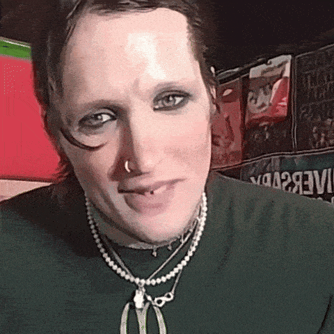 a man wearing a green shirt and a pearl necklace has a piercing in his nose