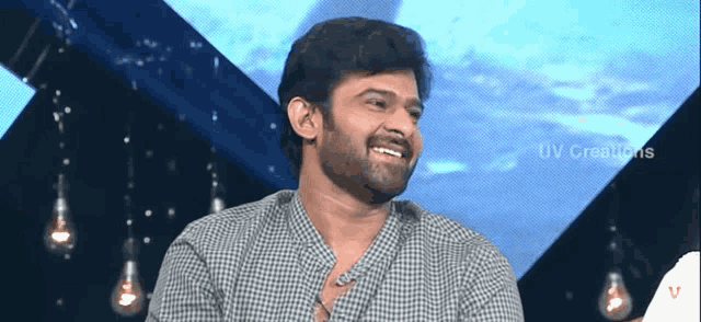 a man with a beard is smiling in front of a blue background with uv creations written on the bottom