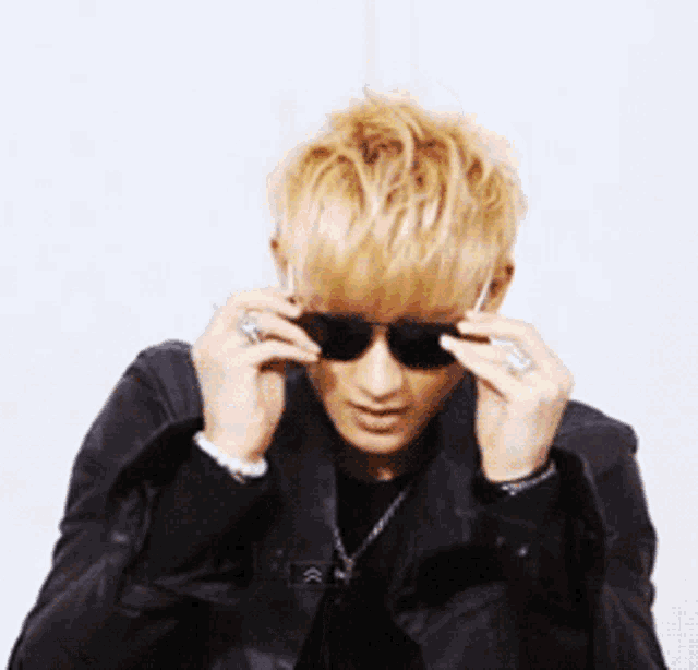 a man wearing sunglasses and a leather jacket looks at the camera