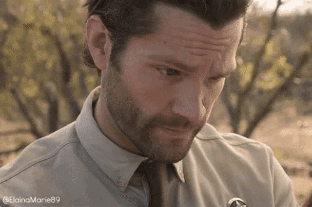 a man with a beard wearing a shirt and tie is looking down