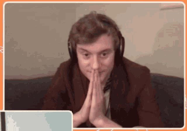 a man wearing headphones is sitting on a couch with his hands folded in front of him .