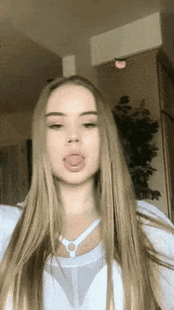 a woman with long blonde hair is sticking her tongue out while wearing a white shirt .