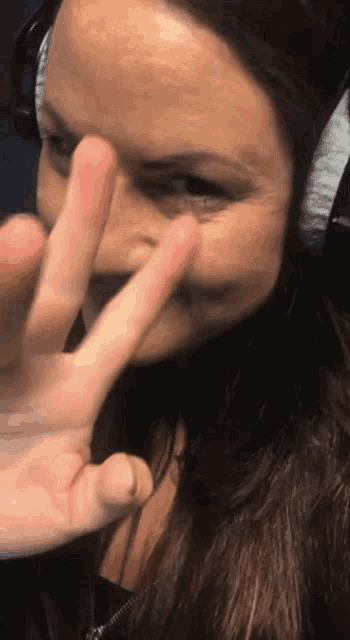 a woman wearing headphones is giving the peace sign