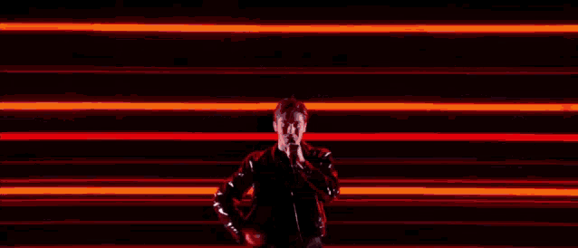 a man in a black jacket is dancing in front of a wall of red lights .