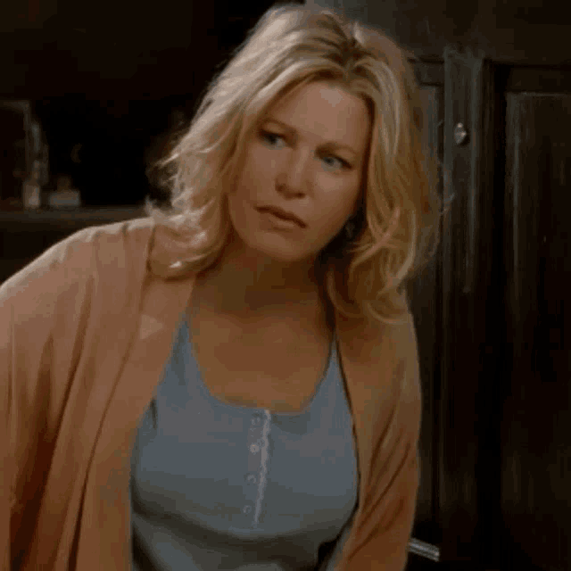 a woman wearing a pink cardigan and a blue tank top looks at the camera