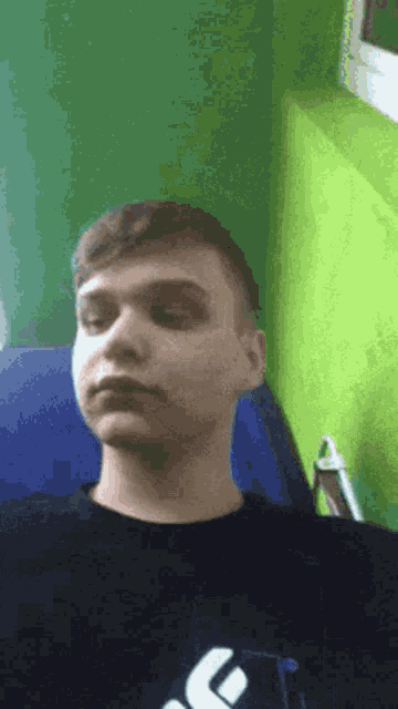a young man is sitting in a chair with his eyes closed and a green wall behind him .