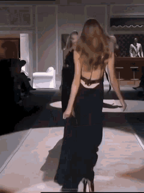 a woman in a black dress is walking on a runway