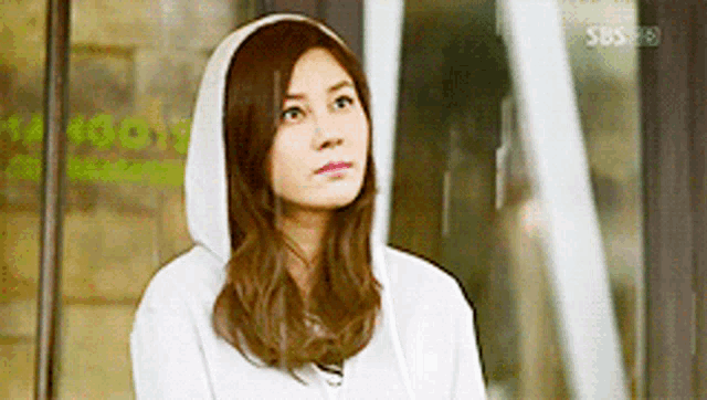 a woman wearing a white hoodie is standing in front of a sbs logo