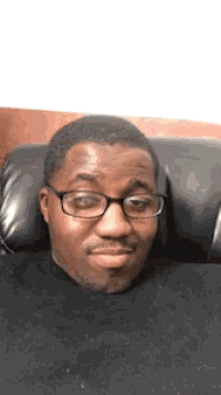 a man wearing glasses and a black sweater is sitting in a chair
