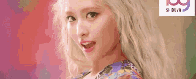 a close up of a woman 's face with long blonde hair and a floral shirt .