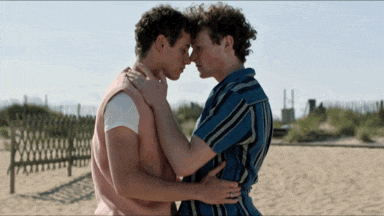 two men are hugging each other on a beach with a fence in the background