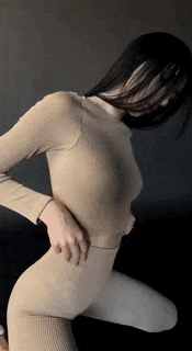 a woman in a tan sweater and white pants is kneeling down and touching her back .