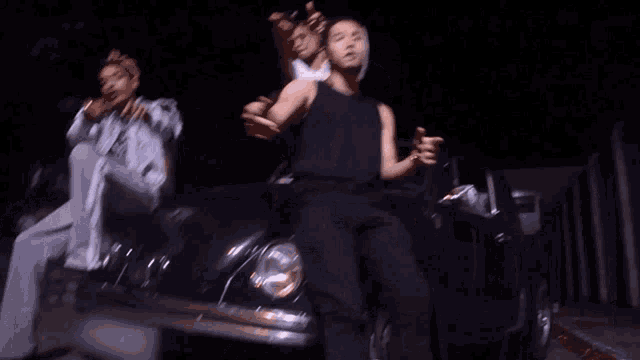 a man in a black tank top is standing in front of a blue car
