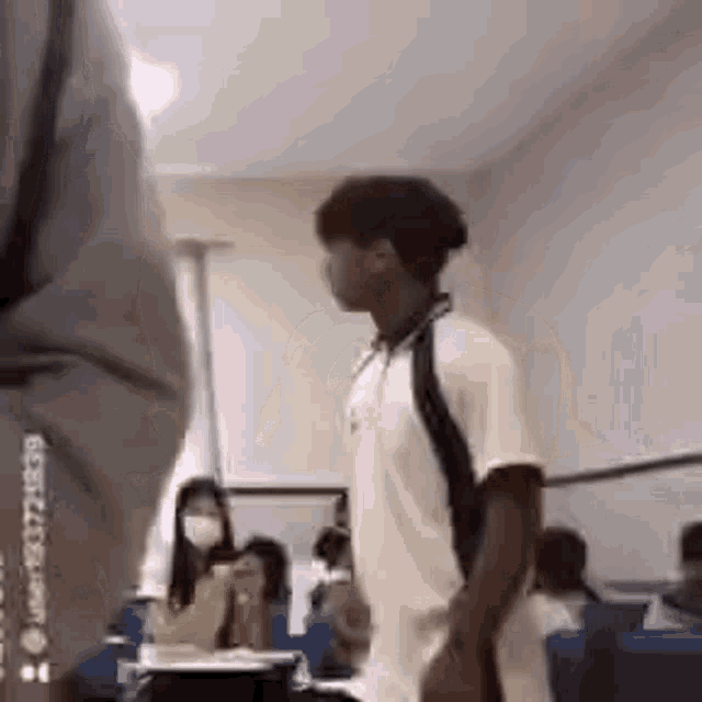 a man wearing a mask is walking in a classroom with other students .