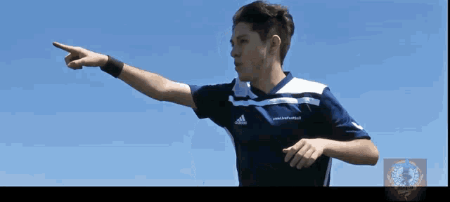 a young man wearing an adidas shirt is pointing to the sky