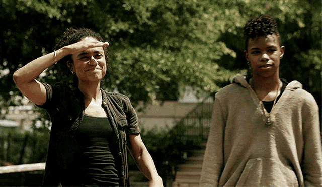 a woman shields her eyes from the sun while standing next to a young boy