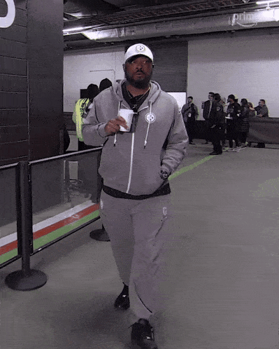 a man wearing a grey hoodie and a white hat is walking in a room with a sign that says prime