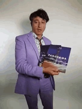 a man in a purple suit is holding a magazine .