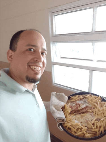 a man holding a pan of food with french fries and meat