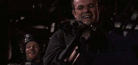 a man in glasses is holding a gun in his hand and smiling .