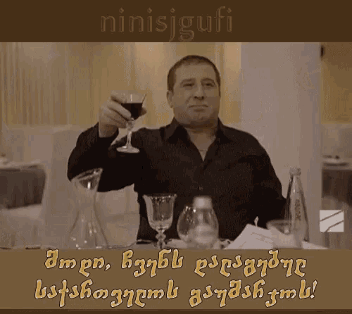a man is holding a glass of wine in front of a sign that says ninisjgufi