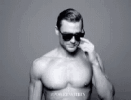 a shirtless man wearing sunglasses is standing in front of a wall .