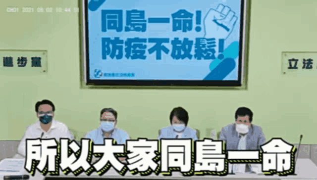 a group of people wearing face masks are sitting at a table in front of a sign with chinese writing
