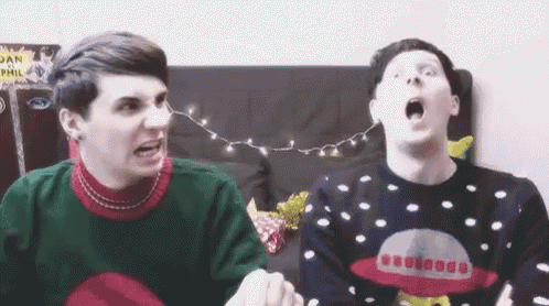 two men wearing ugly christmas sweaters are sitting on a couch and one has his mouth open