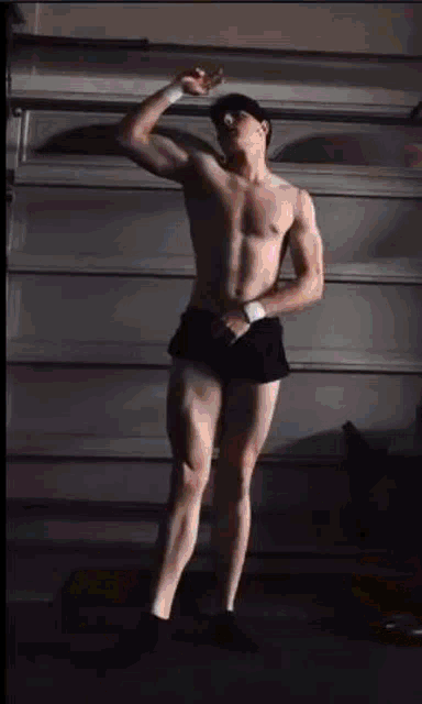 a shirtless man in shorts is standing in front of a garage door