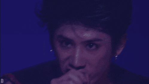 a close up of a man singing into a microphone with the letter d above him