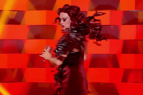 a drag queen is holding a microphone in front of a red wall .