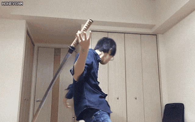 a man in a blue shirt is holding a large sword in a room with a honeycam watermark on the bottom right